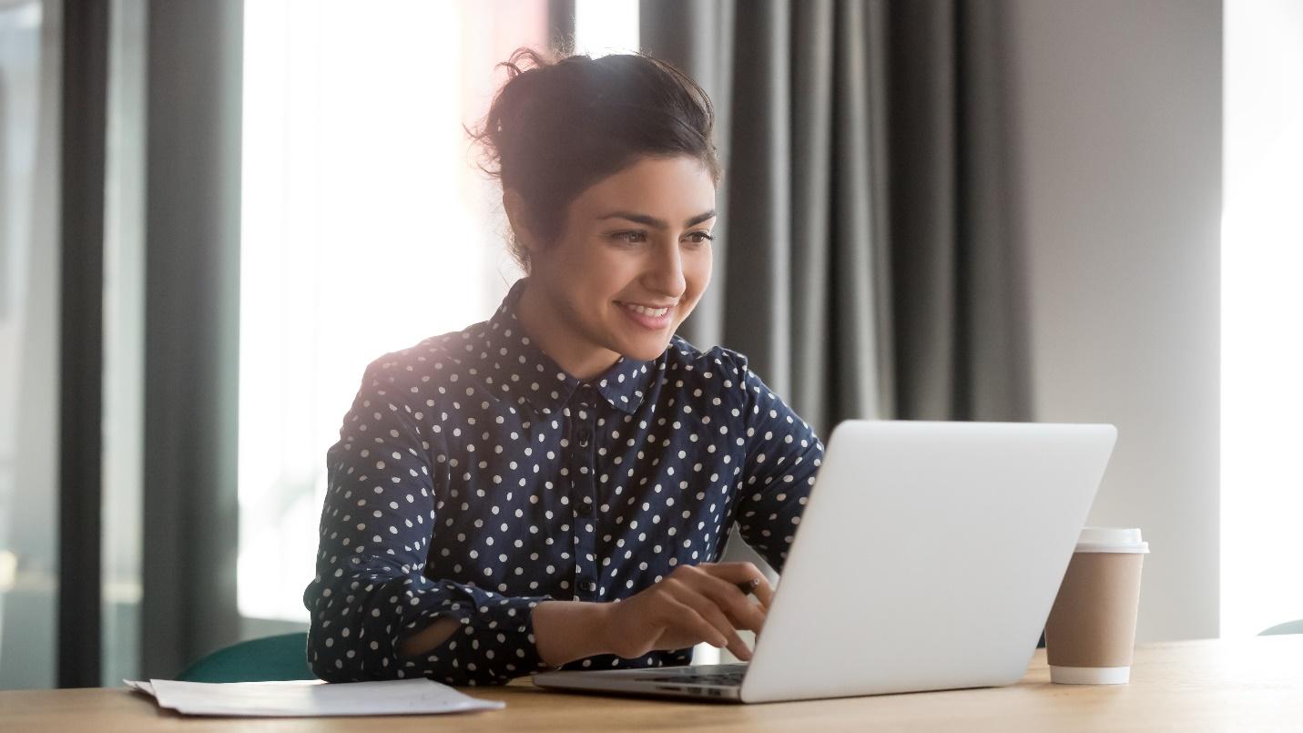 Smiling IT professional in polka dots working alone at a laptop.