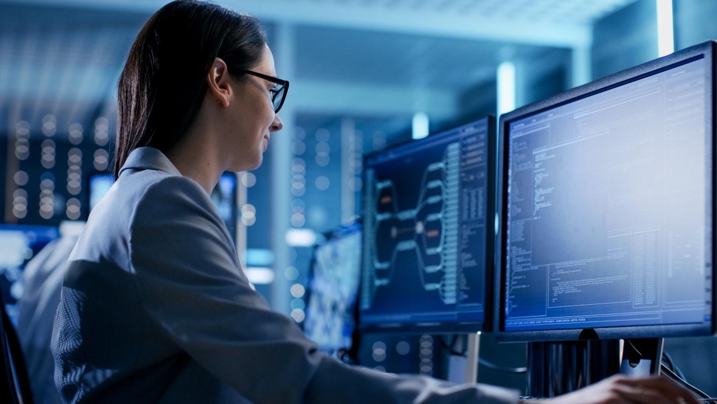 Image of an ethical hacker seated at a desk looking at multiple monitors.