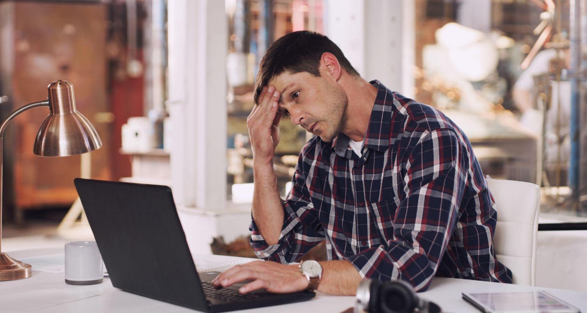 A tired and stressed man at his laptop is overwhelmed by emails.