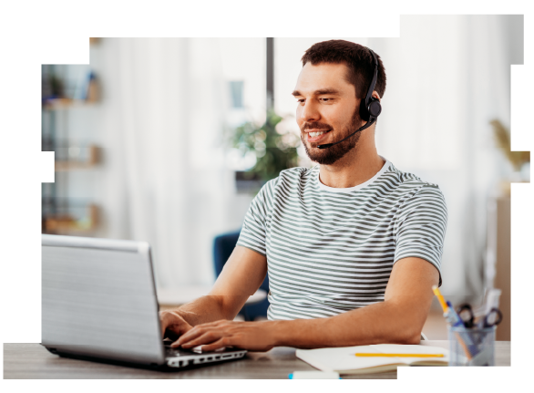 A smiling man wearing a headset and sitting at a table typing on a laptop