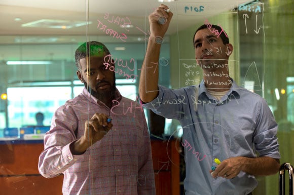 Two men writing equations on a glass wall