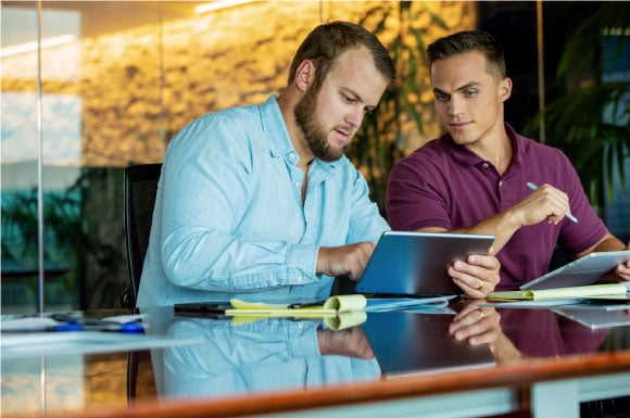 Two men sitting at a conference table looking at a tablet